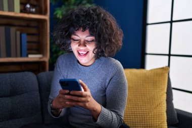 Evdeki kanepede oturan akıllı telefon kullanan genç, güzel İspanyol kadın.