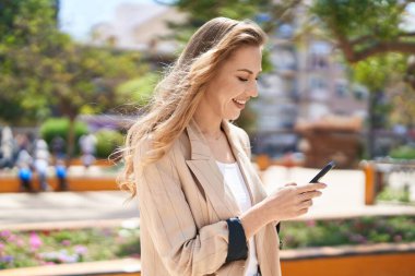 Parkta akıllı telefon kullanan, kendine güvenen genç sarışın kadın.