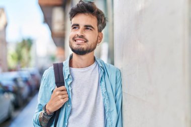 Young hispanic man student smiling confident wearing backpack at street