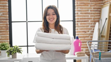 Çamaşırhanede katlanmış havlularla gülümseyen güzel İspanyol kadın.