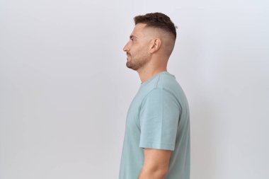 Hispanic man with beard standing over white background looking to side, relax profile pose with natural face and confident smile. 