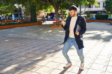 Genç İspanyol adam parkta dizüstü bilgisayar tutuyor.