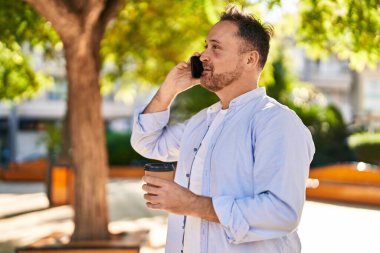 Kafkasyalı genç adam akıllı telefondan konuşuyor parkta kahve içiyor.