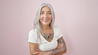 Orta yaşlı, gri saçlı, kolları çapraz duran, izole edilmiş pembe arka planı olan bir kadın.