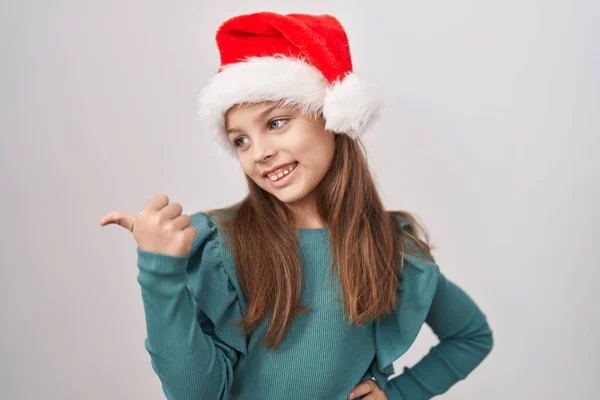 Little Caucasian Girl Wearing Christmas Hat Pointing Thumb Side Smiling — ストック写真