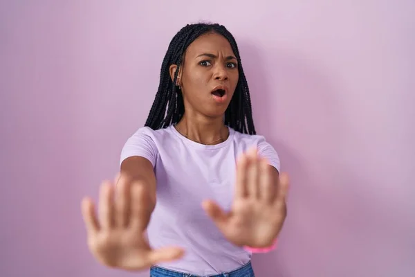 戴着辫子站在粉色背景上的非洲裔美国妇女害怕 害怕的表情 用手停止手势 震惊地大叫 恐慌概念 — 图库照片