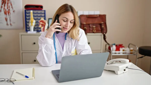 年轻美丽的惊慌失措的女医生在诊所用笔记本电脑用智能手机交谈 — 图库照片