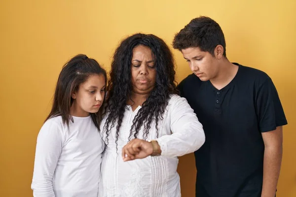 母親と娘と息子の家族が黄色の背景の上に立っています時間をチェック上の手首の腕時計 リラックスして自信 — ストック写真