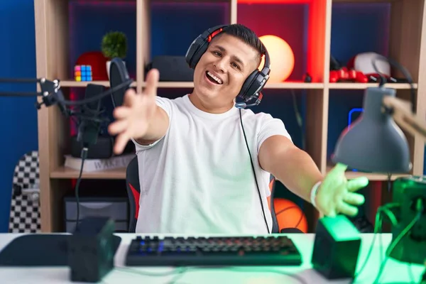 抱擁のために腕を開いて笑顔カメラを見てビデオゲームをプレイする若いヒスパニック系の男 幸せを受け入れる陽気な表情 — ストック写真