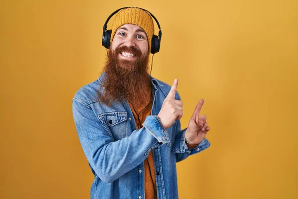 長い髭を生やした白人男性がヘッドフォンを使用して音楽を聞いて笑顔とカメラを見て2本の手と指で側面を指して — ストック写真