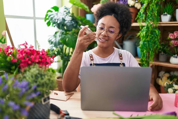 African american woman florist talking on smartphone using laptop at flower shop