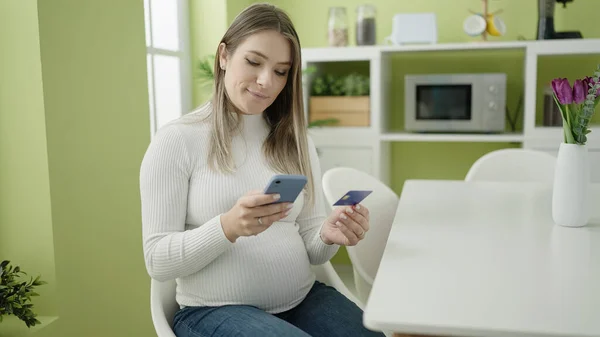 带着智能手机和信用卡购物的年轻孕妇坐在餐厅的桌子上 — 图库照片