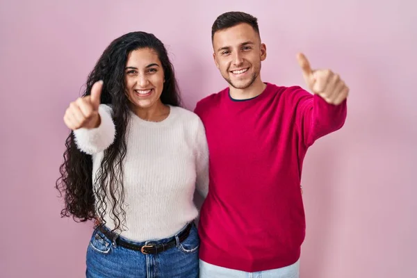 Young Hispanic Couple Standing Pink Background Approving Doing Positive Gesture — Fotografia de Stock