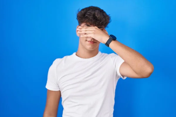 Adolescente Hispânico Sobre Fundo Azul Cobrindo Olhos Com Mão Olhando — Fotografia de Stock