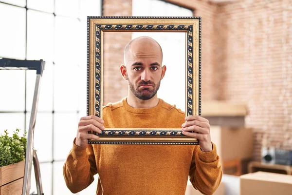 年轻的秃头男人带着胡子搬到了一个新家 把脸放进了老式的镜框里 脸上带着严肃的表情 简单而自然地看着相机 — 图库照片
