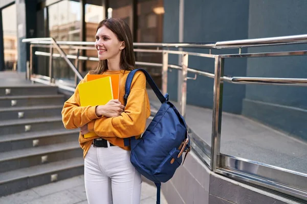 Young blonde woman student wearing backpack holding books at university