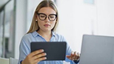 Genç sarışın iş kadını ofiste dizüstü bilgisayar ve dokunmatik ped kullanıyor.