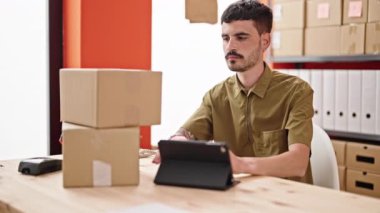 Latin kökenli genç bir iş adamı. Ofiste dokunmatik ped kullanarak paketleri tutuyor.