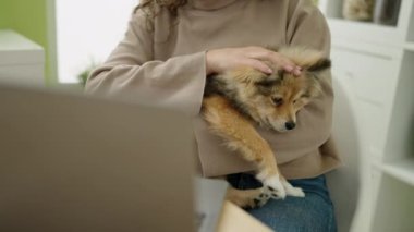 Yemek odasında laptopunu kullanan köpekli genç İspanyol kadın.