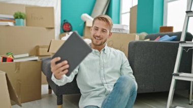 Kafkasyalı genç bir adam yeni evinde yerde otururken görüntülü konuşma yapıyor.