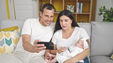 Üç kişilik aile akıllı telefon kullanıyor. Evdeki kanepede oturup video izliyorlar.