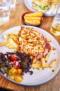  Lezzetli bir tabak İtalyan lazanyası kızarmış patates ve salata ahşap yüzeyi.