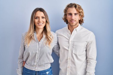 Mavi arka planda mutlu ve havalı bir gülümsemeyle duran genç bir çift. şanslı kişi. 