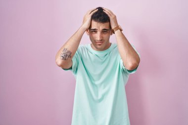 Pembe arka planda duran yakışıklı İspanyol adam acı ve migrenden dolayı çaresiz ve stresli baş ağrısı çekiyor. Eller başının üstünde.. 