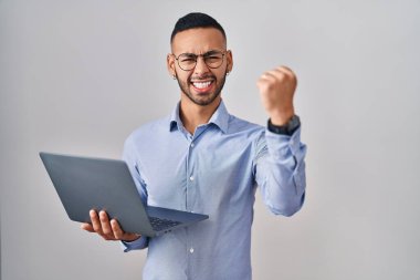 Genç İspanyol adam bilgisayar kullanıyor kızgın ve kızgın yumruğunu kaldırıyor ve öfkeyle bağırıyor. öfke ve agresif konsept. 