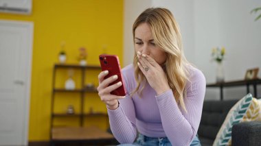 Genç, güzel, İspanyol bir kadın akıllı telefon kullanıyor. Evde üzgün görünüyor.