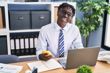 Ofiste bilgisayar ve akıllı telefon kullanan Afro-Amerikalı iş adamı.