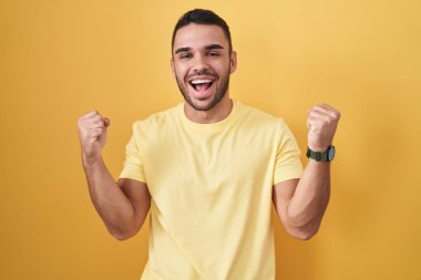 Young hispanic man standing over yellow background celebrating surprised and amazed for success with arms raised and eyes closed. winner concept. 