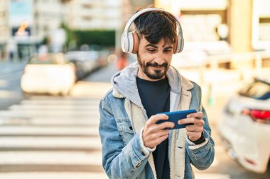 Young hispanic man smiling confident playing video game at street
