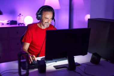 Middle age man streamer playing video game using computer at gaming room