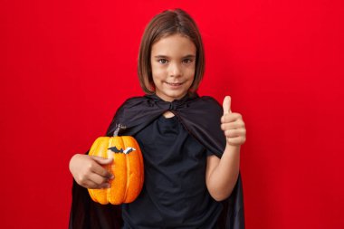 Küçük İspanyol çocuk pelerin giyiyor ve elinde cadılar bayramı balkabağı kabağı tutuyor gururla bağırıyor, zaferi kutluyor ve başarıyı kollarını kaldırarak kutluyor. 