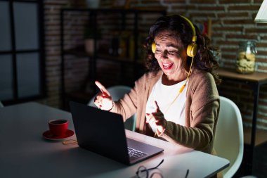 Orta yaşlı İspanyol kadın gece evde dizüstü bilgisayar kullanarak dans ediyor.