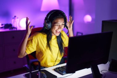 Genç, güzel, Latin bir kadın oyuncu oyun odasında video oyunu oynuyor.