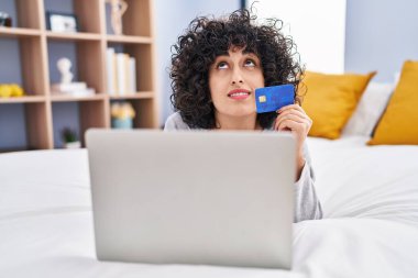 Young middle east woman using laptop and credit card lying on bed at bedroom