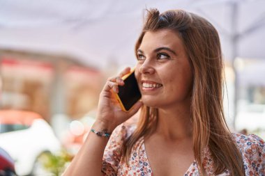 Gülümseyen genç bir kadın caddedeki akıllı telefondan konuşuyor.