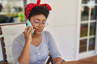 Afrika kökenli Amerikalı bir kadın akıllı telefonuyla ev terasındaki masada oturuyor.