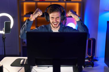 Beyazlı genç adam oyun odasında video oyunu oynuyor ve kazanan ifadesini kullanıyor.