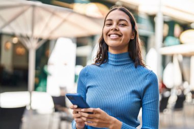 Genç Afro-Amerikalı kadın sokakta akıllı telefon kullanarak gülümsüyor.