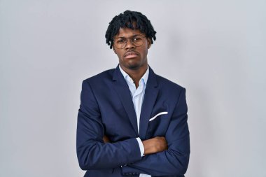 Rasta saçlı genç Afrikalı bir adam beyaz arka plan kuşkucu ve gergin, yüzünde çapraz kollu tasvip etmeyen bir ifade olan iş ceketi giyiyor. negatif kişi. 