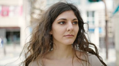 Young beautiful hispanic woman looking to the side with serious expression at street