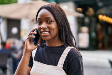 Genç Afrikalı Amerikalı kadın gülümsüyor. Kendine güveni tam. Sokakta akıllı telefondan konuşuyor.