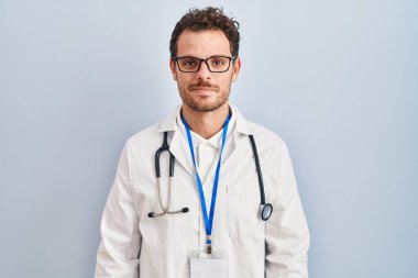 Doktor üniforması giyen ve steteskop takan İspanyol genç adam yüzünde ciddi bir ifadeyle rahatladı. Basit ve doğal bir şekilde kameraya bakıyorsun.. 