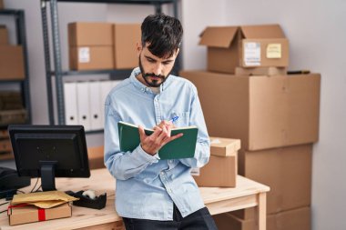 Young hispanic man ecommerce business worker writing on notebook at office