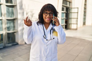 Young beautiful latin woman doctor smiling confident talking on smartphone at hospital