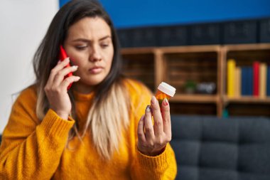 Young beautiful plus size woman talking on smartphone holding pills at home