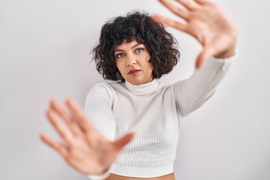 Kıvırcık saçlı İspanyol kadın izole edilmiş arka planda duruyor. El ve parmakları kullanarak çerçeve yapıyor. 